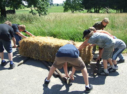 Strohballenspiele: einen Strohballen auf Hölzern in ein Ziel bewegen.