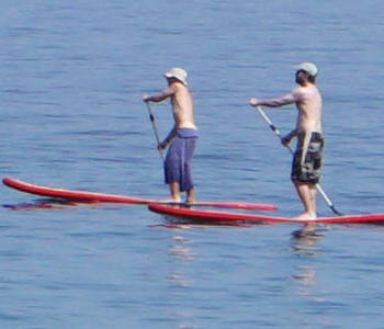 Stehend auf einem Stand-up Paddle Board wird eine oder mehrere Bojen umfahren.